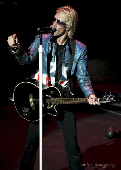 Close up production image of a musician singing and playing guitar on stage with The Bon Jovi Experience